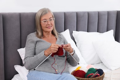 Photo of Smiling senior woman knitting on bed at home