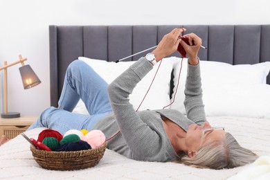 Photo of Beautiful senior woman knitting on bed at home