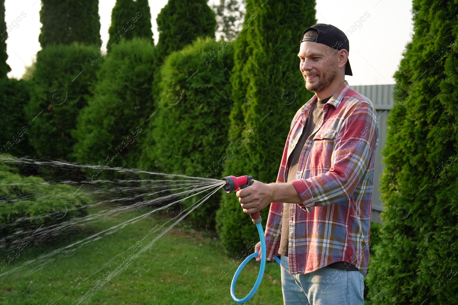 Photo of Man watering lawn with hose in backyard