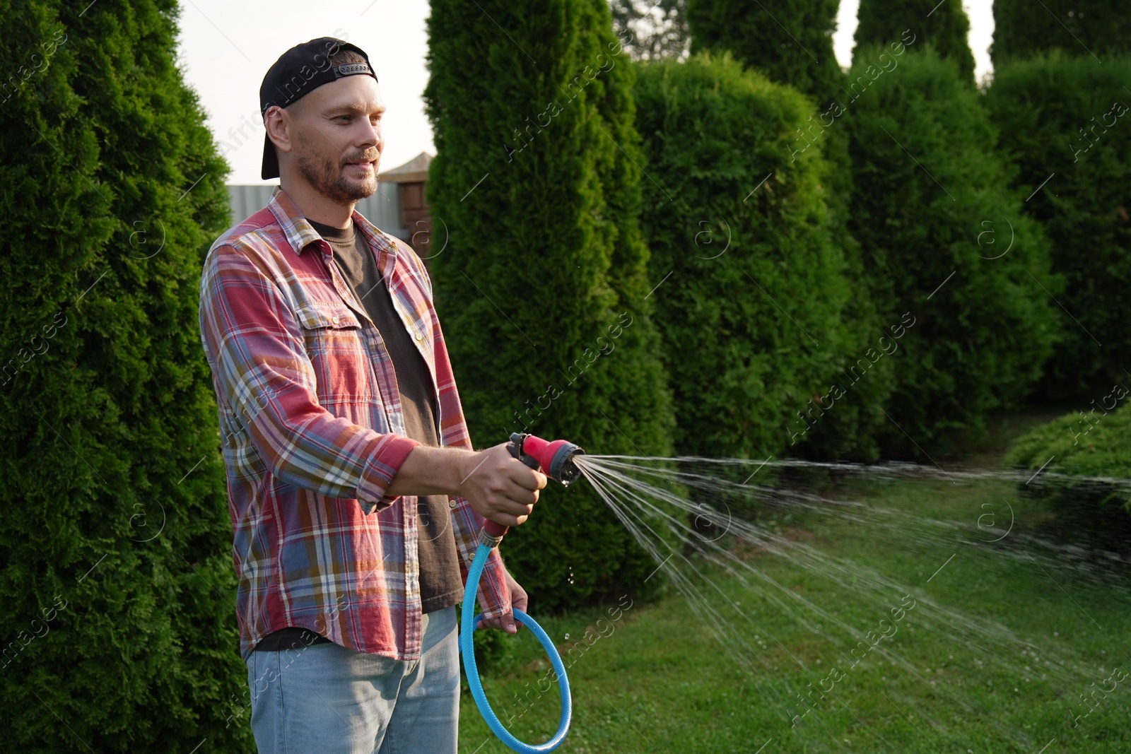 Photo of Man watering lawn with hose in backyard