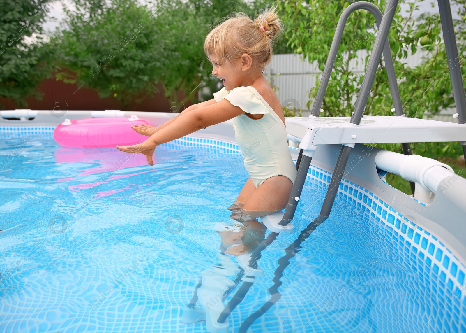 Photo of Happy girl getting into swimming pool by ladder outdoors