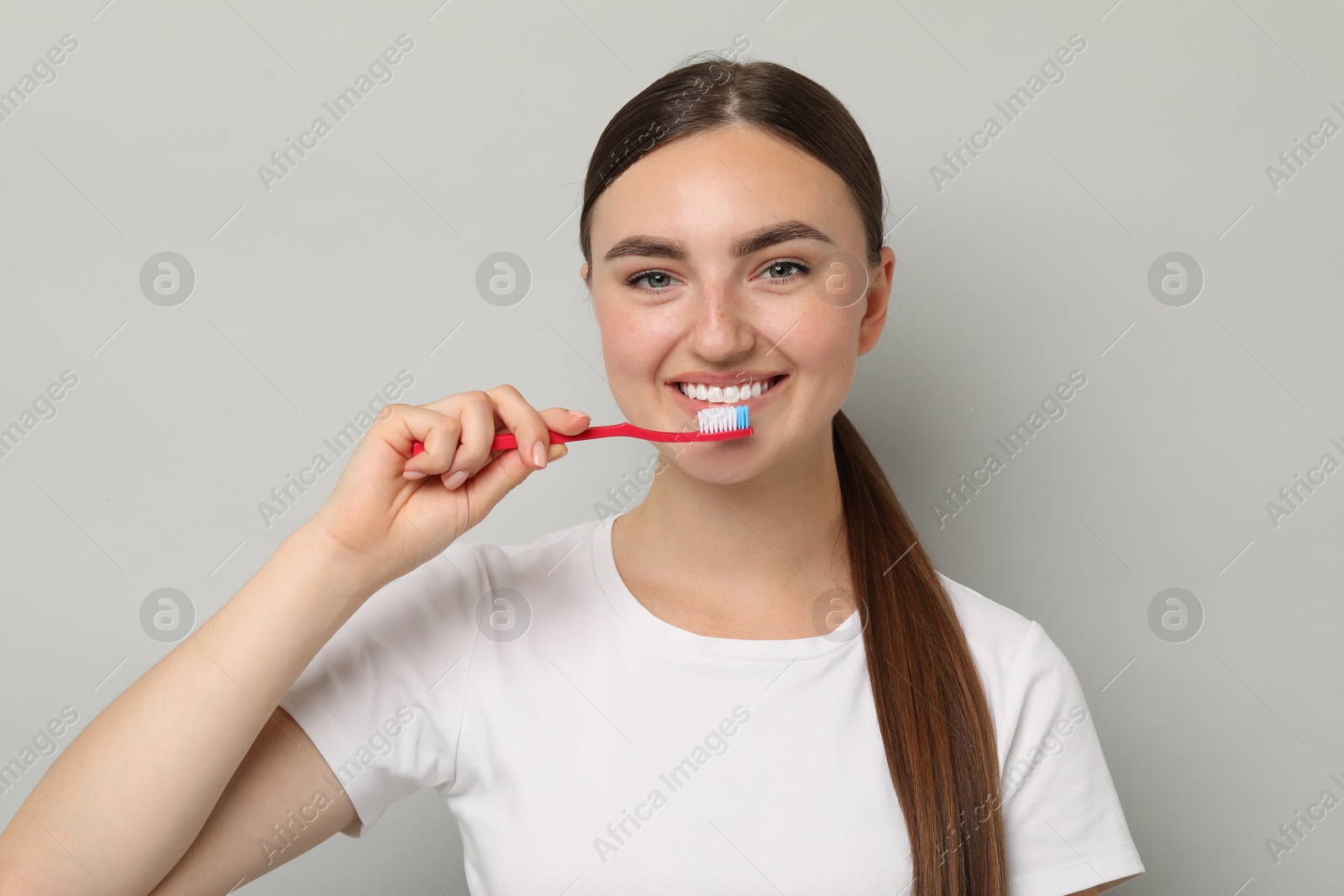 Photo of Beautiful woman brushing her teeth on gray background