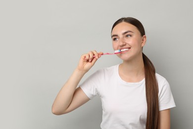 Photo of Beautiful woman brushing her teeth on gray background, space for text