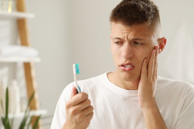 Photo of Young man with toothbrush suffering from toothache in bathroom