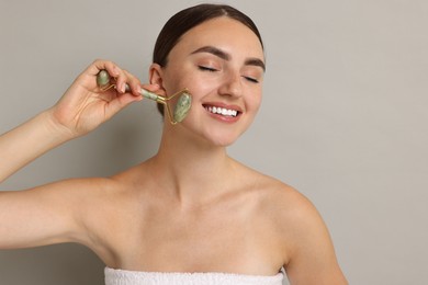 Photo of Beautiful young woman doing facial massage with roller on grey background