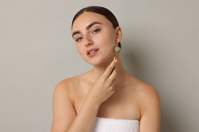 Photo of Beautiful young woman doing facial massage with roller on grey background