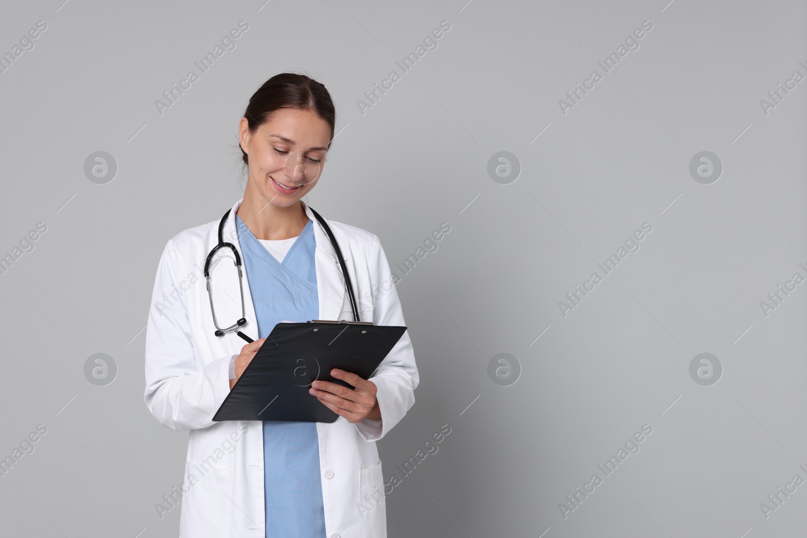 Photo of Nurse in medical uniform with stethoscope and clipboard on grey background, space for text