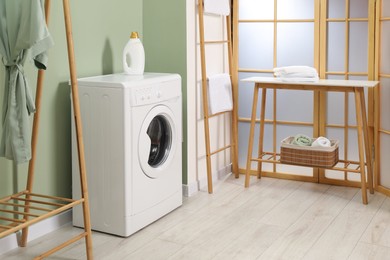 Photo of Washing machine, towels and detergent in laundry room