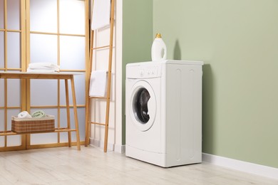 Photo of Washing machine, towels and detergent in laundry room