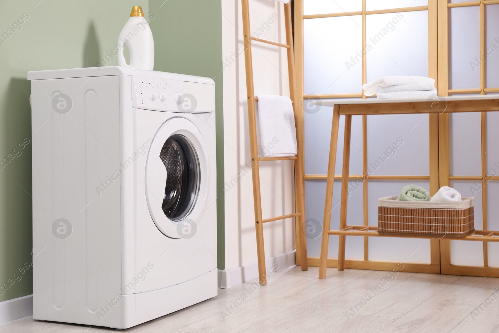 Photo of Washing machine, towels and detergent in laundry room