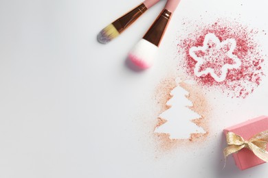 Christmas decorations made of powder and blush, gift box and makeup brushes on white background, flat lay. Space for text