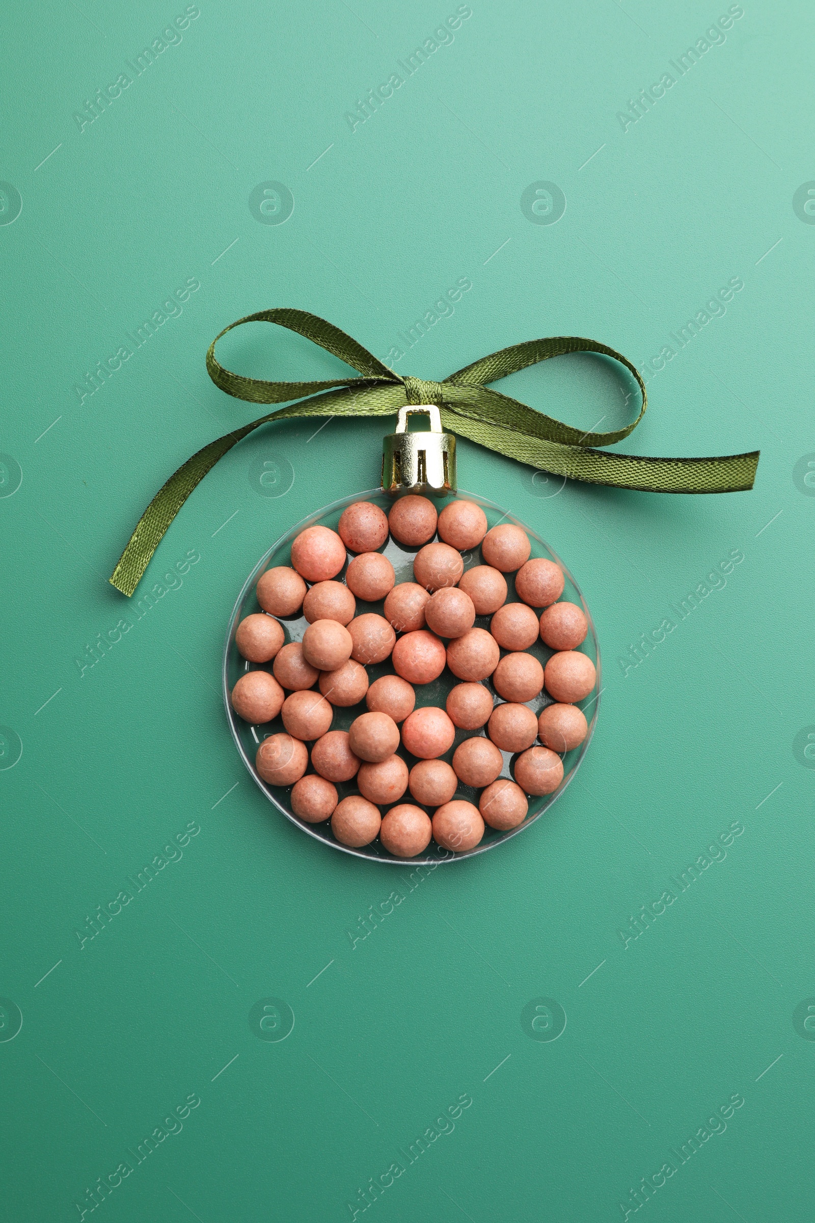 Photo of Christmas ball made of cosmetic product and bow on green background, top view