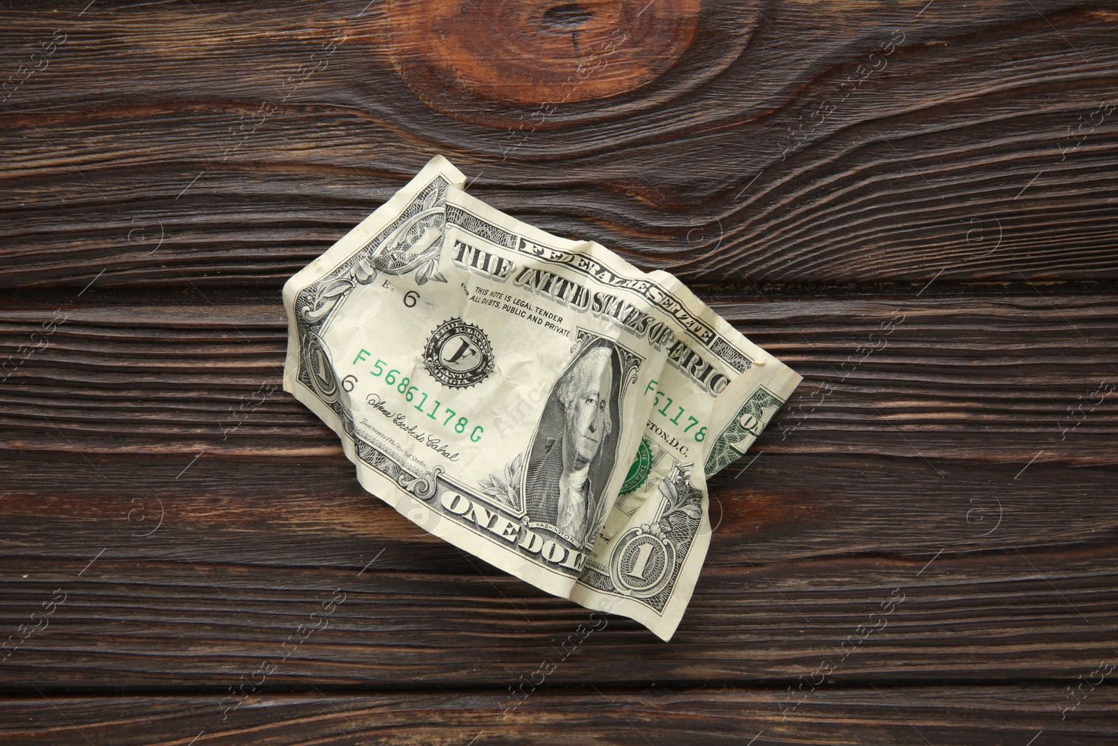 Photo of One crumpled dollar banknote on wooden table, top view