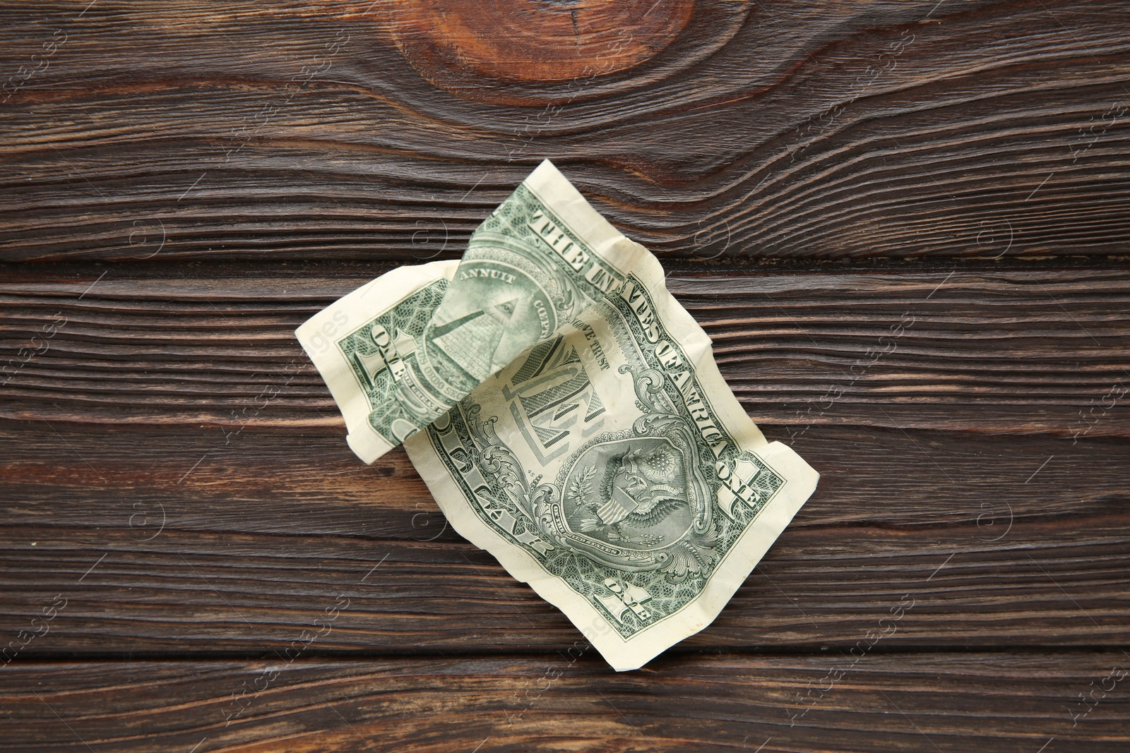 Photo of One crumpled dollar banknote on wooden table, top view