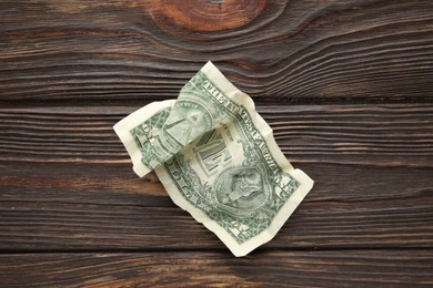 Photo of One crumpled dollar banknote on wooden table, top view