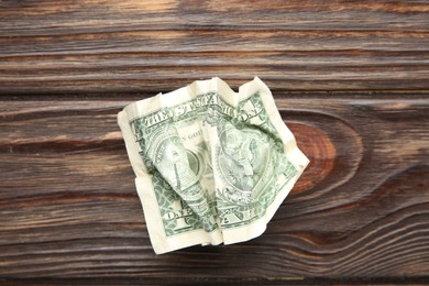 Photo of One crumpled dollar banknote on wooden table, top view