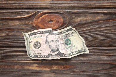 Photo of One crumpled dollar banknote on wooden table, top view