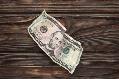 Photo of One crumpled dollar banknote on wooden table, top view