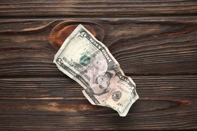 Photo of One crumpled dollar banknote on wooden table, top view