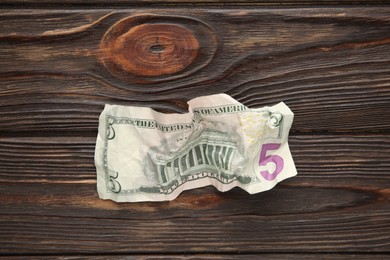 Photo of One crumpled dollar banknote on wooden table, top view