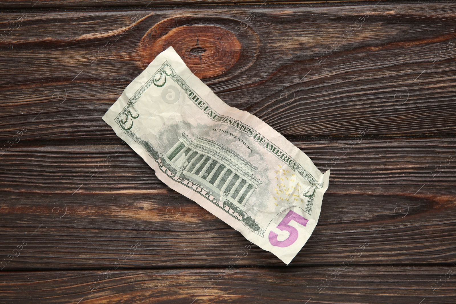 Photo of One crumpled dollar banknote on wooden table, top view