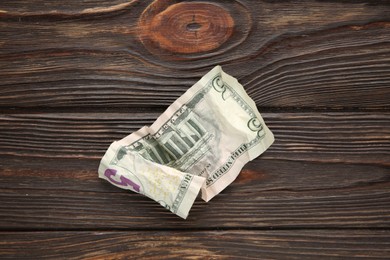 Photo of One crumpled dollar banknote on wooden table, top view