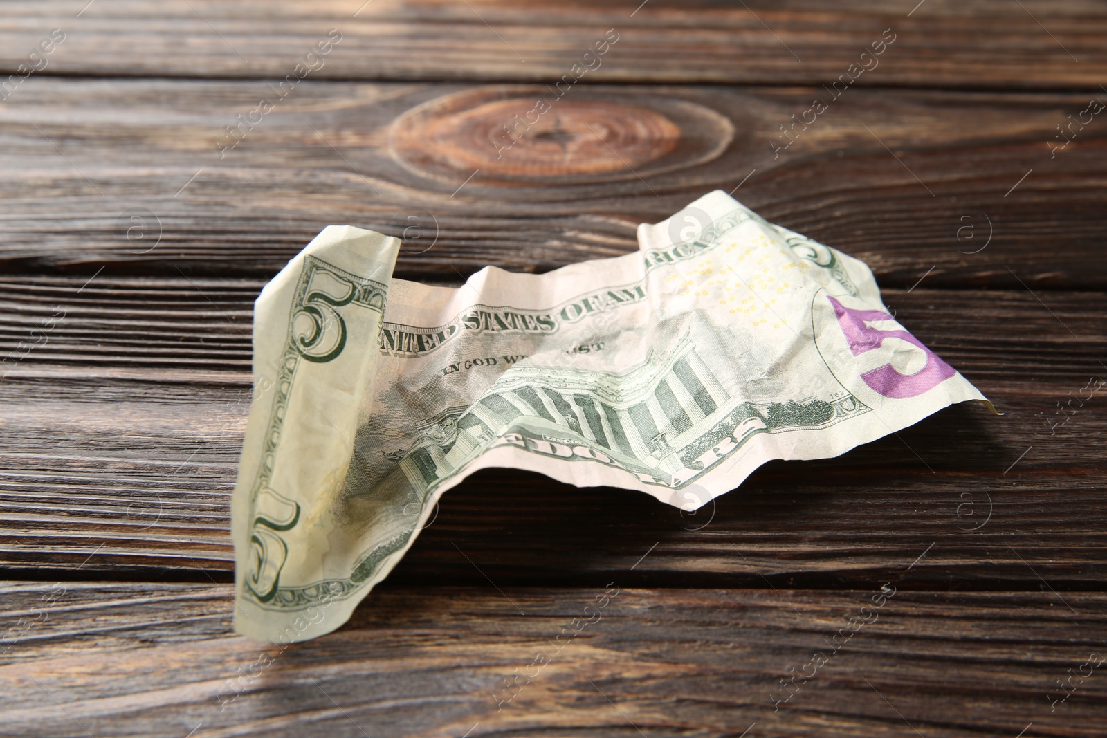 Photo of One crumpled dollar banknote on wooden table, closeup