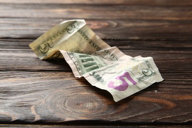 Photo of One crumpled dollar banknote on wooden table, closeup