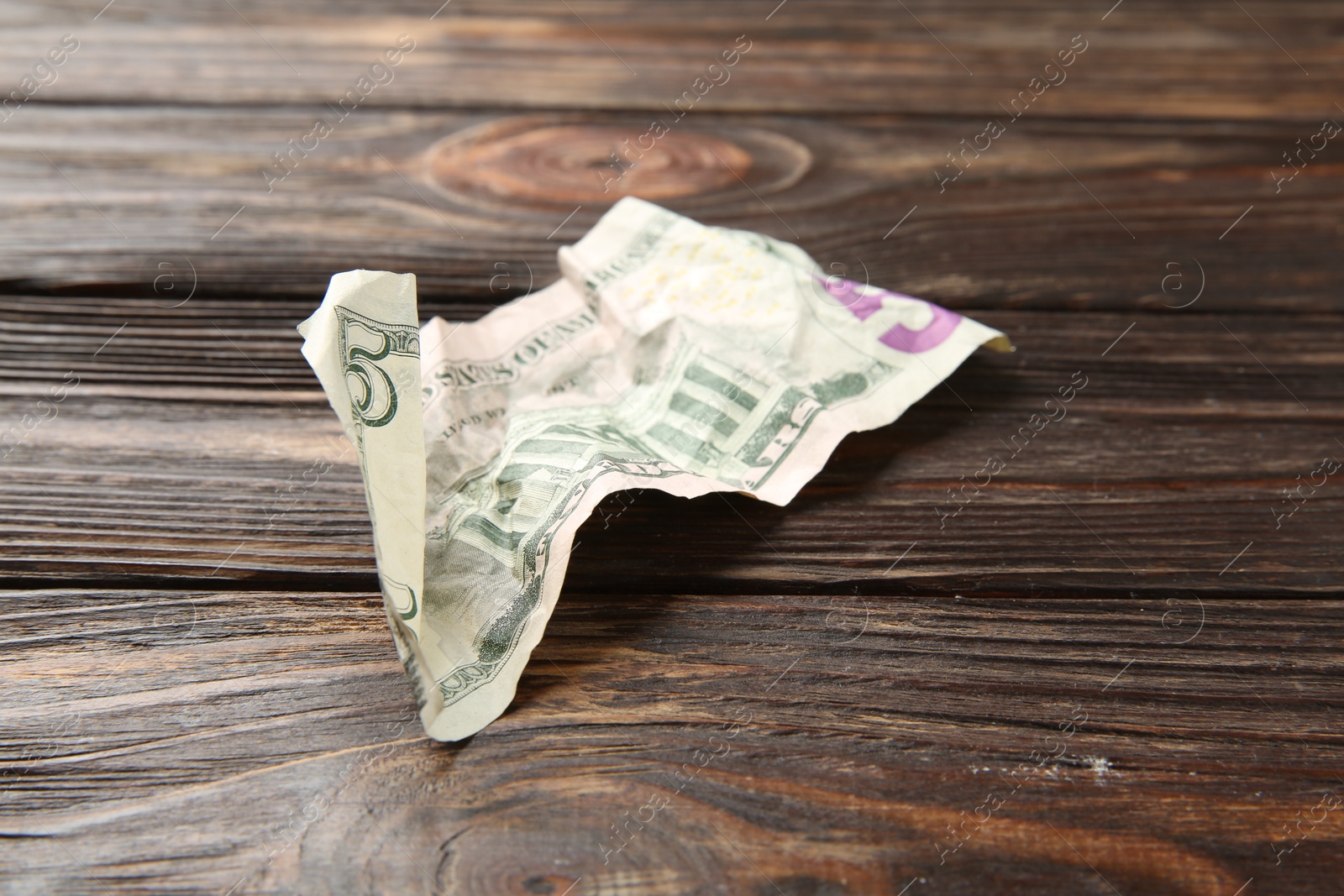 Photo of One crumpled dollar banknote on wooden table, closeup