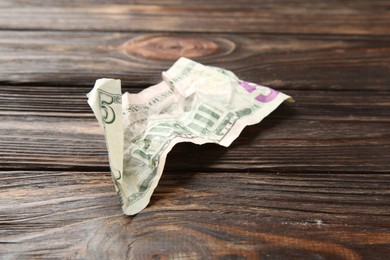 Photo of One crumpled dollar banknote on wooden table, closeup