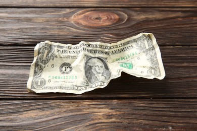 Photo of One crumpled dollar banknote on wooden table, closeup