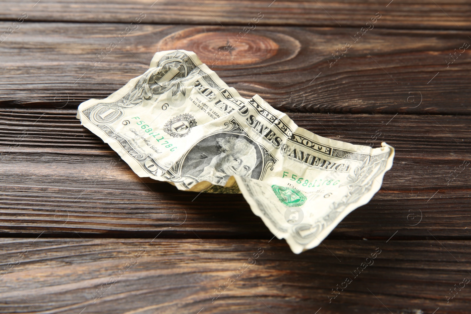 Photo of One crumpled dollar banknote on wooden table, closeup