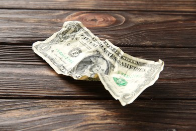 Photo of One crumpled dollar banknote on wooden table, closeup