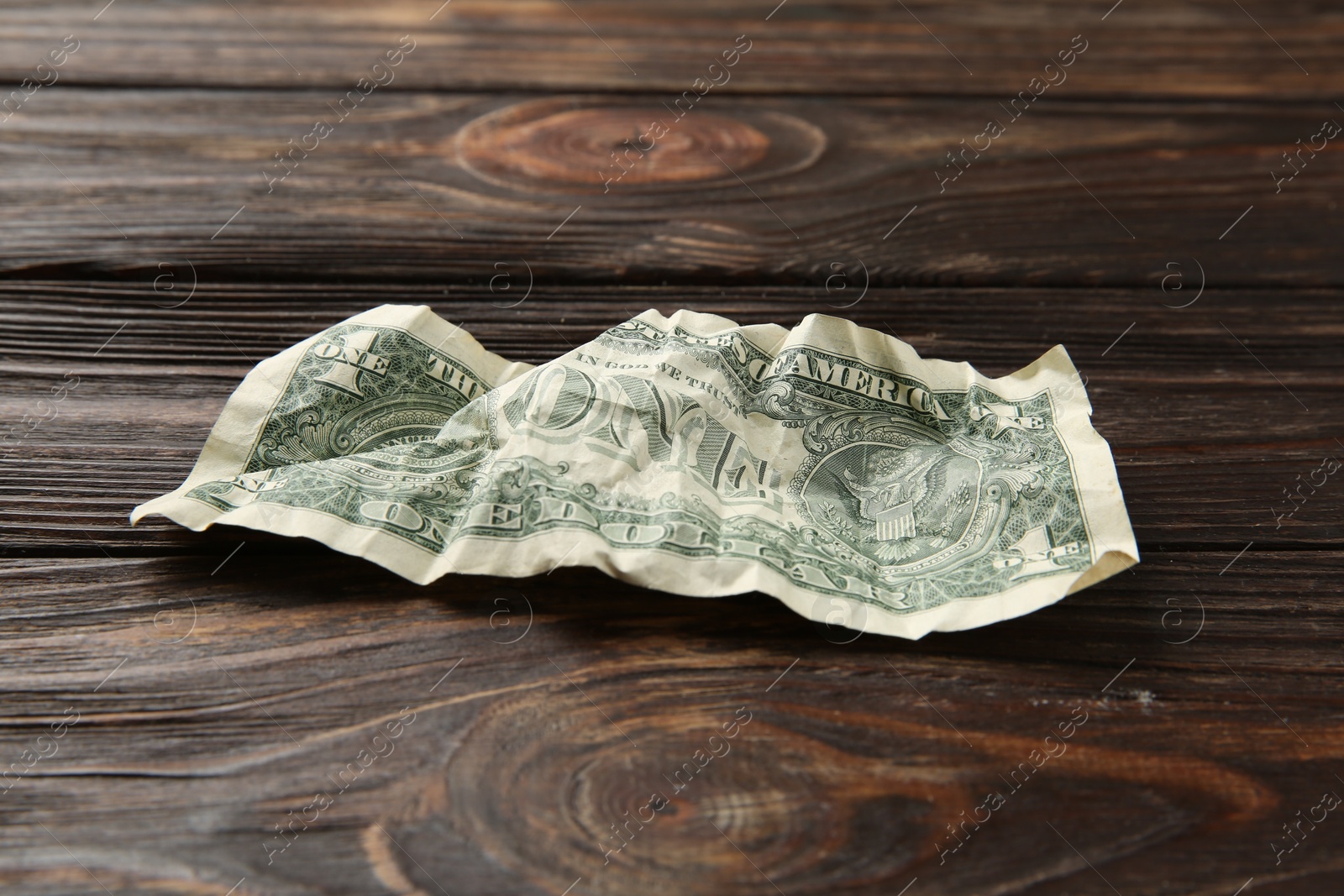 Photo of One crumpled dollar banknote on wooden table, closeup