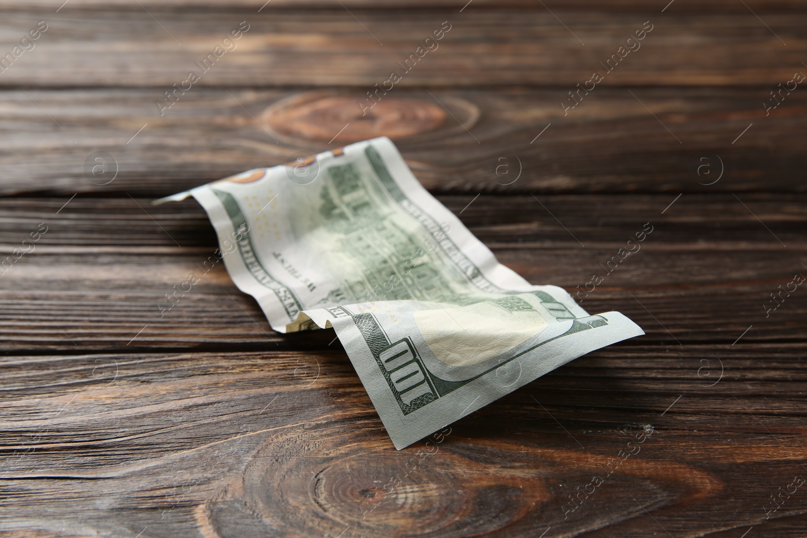 Photo of One crumpled dollar banknote on wooden table, closeup