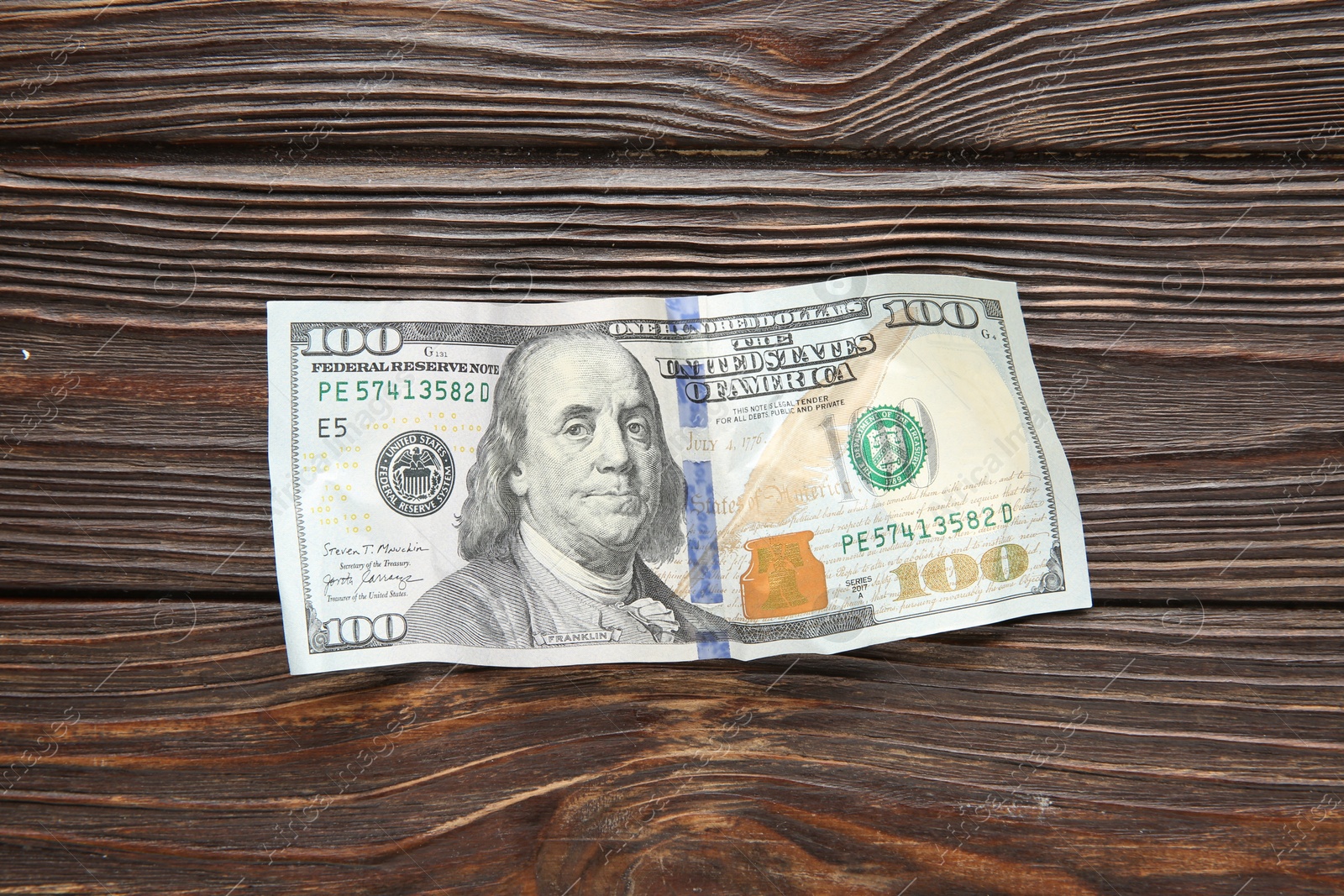 Photo of One crumpled dollar banknote on wooden table, top view