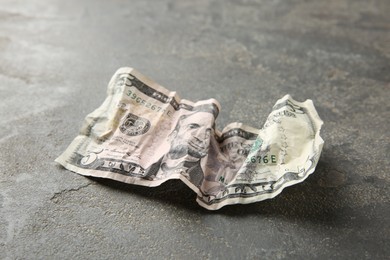 Photo of One crumpled dollar banknote on grey table, closeup