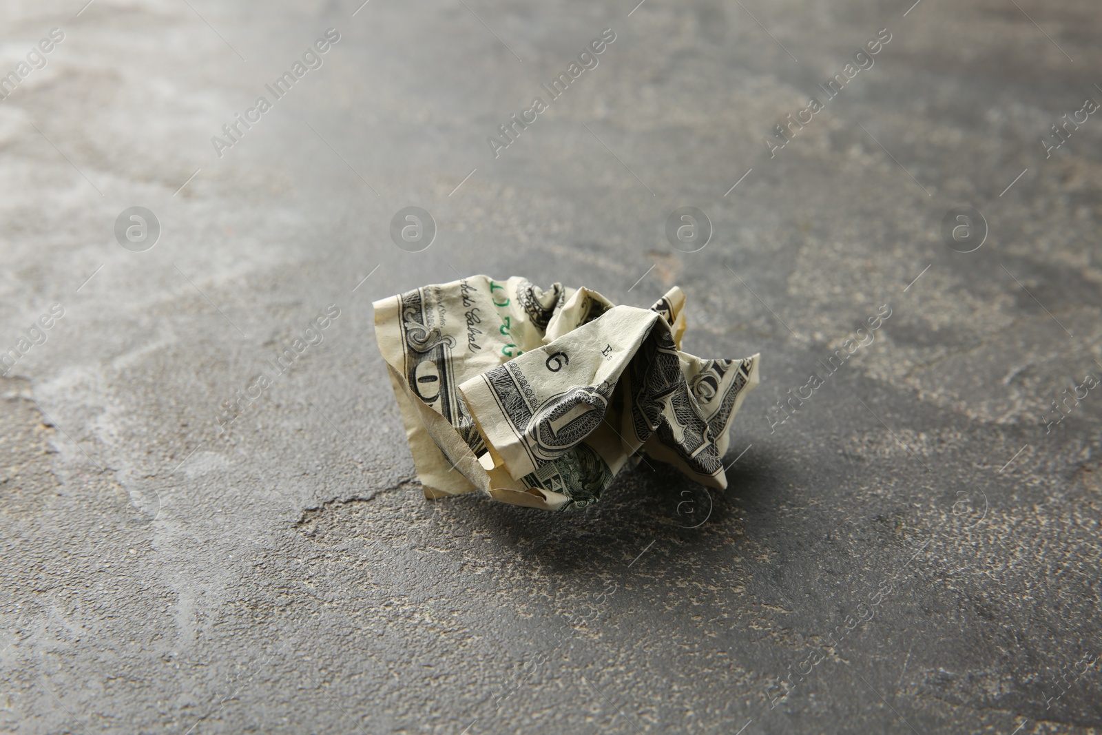 Photo of One crumpled dollar banknote on grey table, closeup