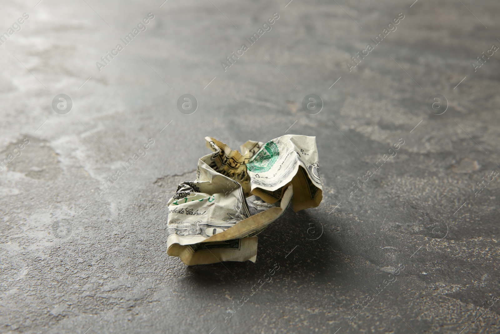 Photo of One crumpled dollar banknote on grey table, closeup