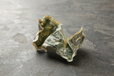 Photo of One crumpled dollar banknote on grey table, closeup