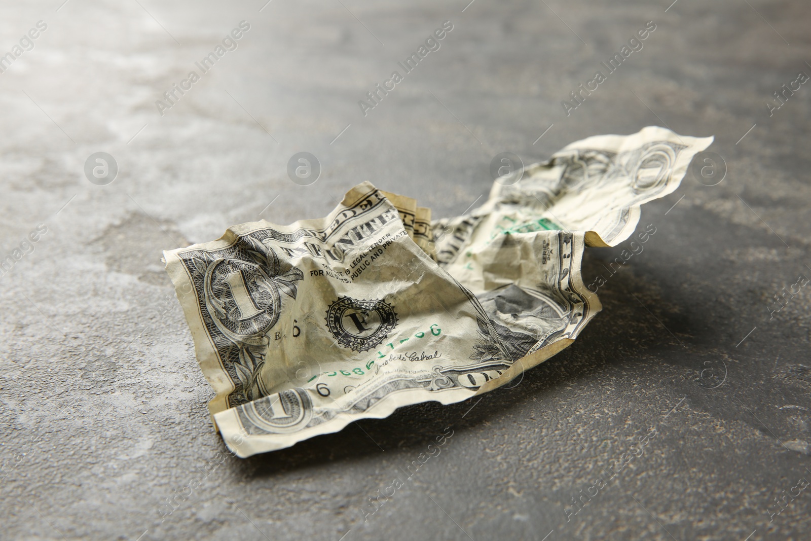 Photo of One crumpled dollar banknote on grey table, closeup