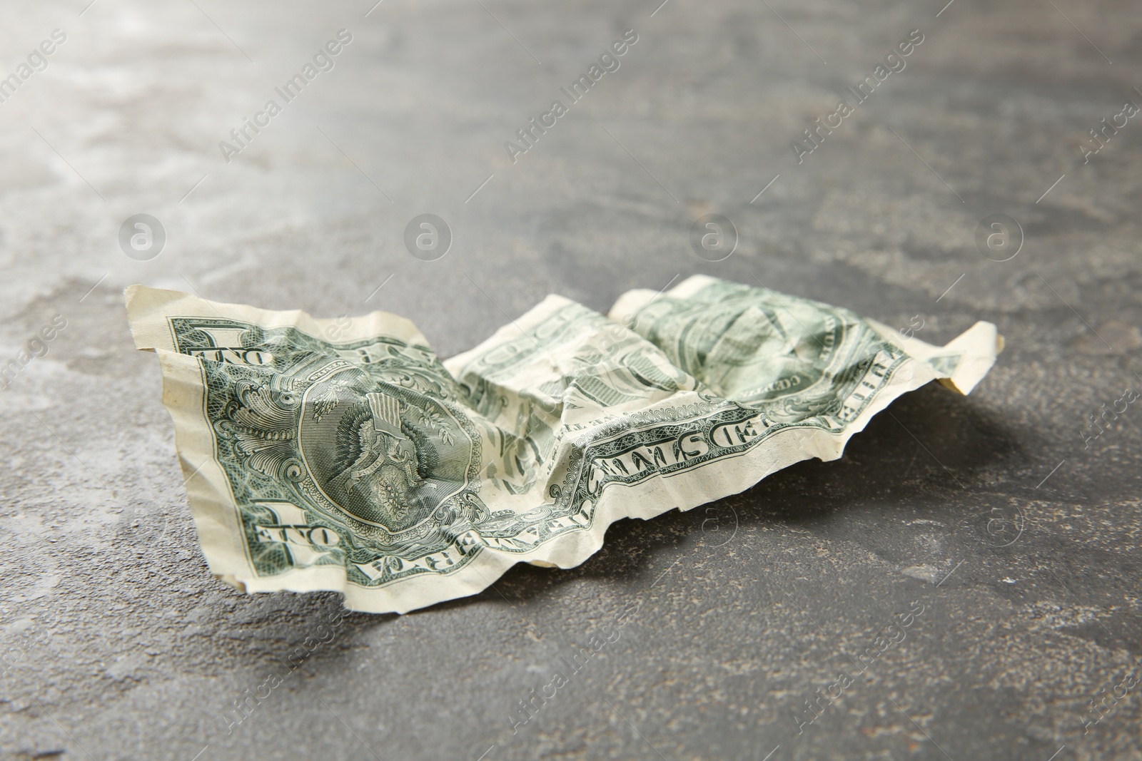 Photo of One crumpled dollar banknote on grey table, closeup