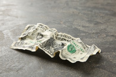 Photo of One crumpled dollar banknote on grey table, closeup