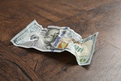 Photo of One crumpled dollar banknote on wooden table, closeup