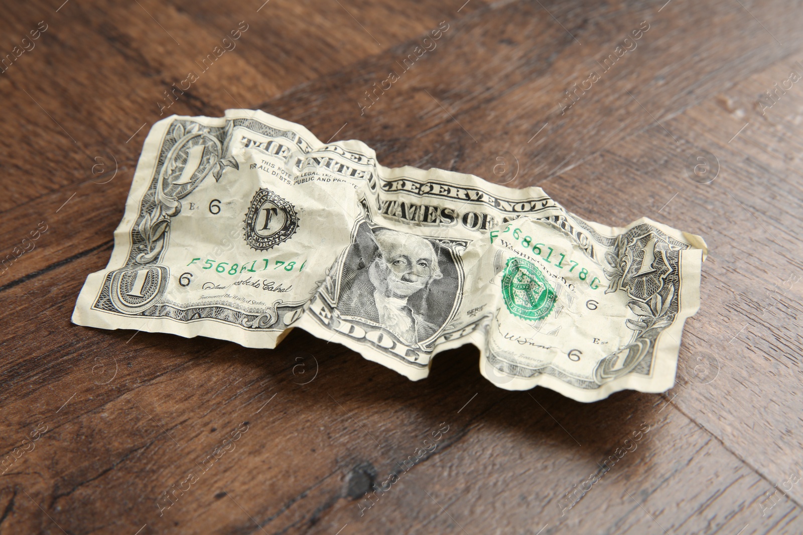 Photo of One crumpled dollar banknote on wooden table, closeup