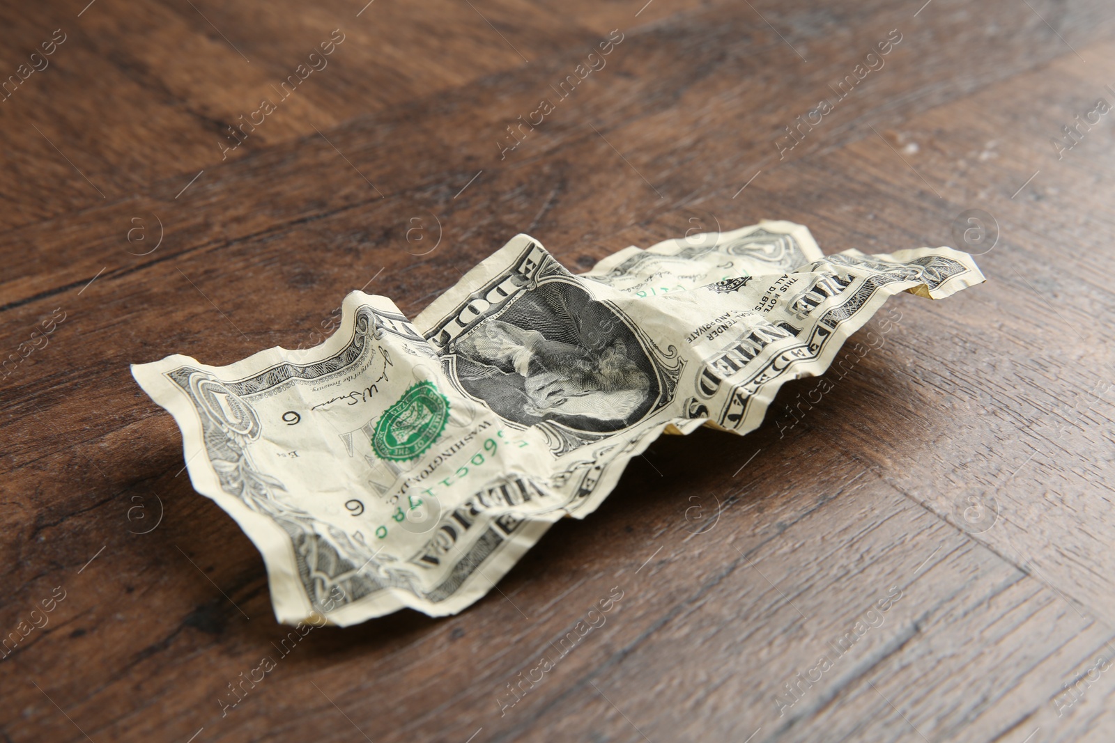 Photo of One crumpled dollar banknote on wooden table, closeup