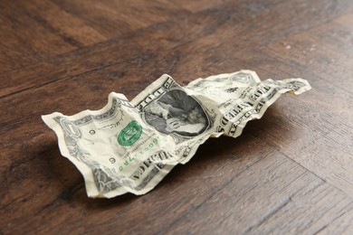 Photo of One crumpled dollar banknote on wooden table, closeup