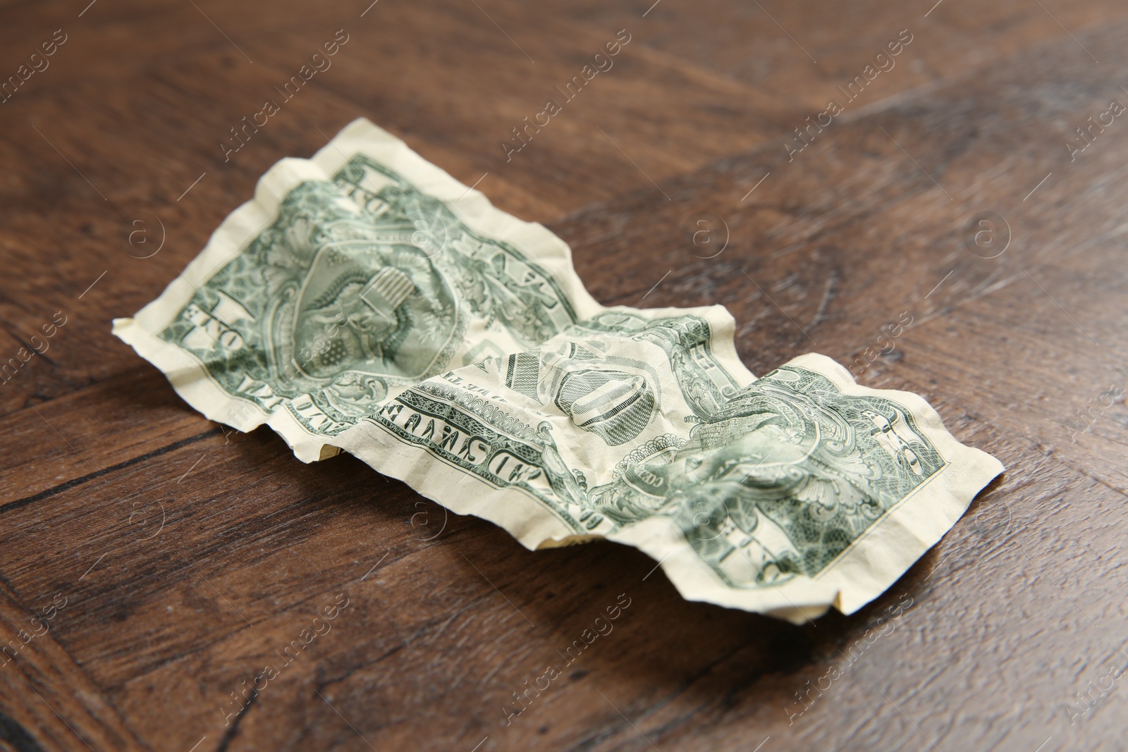 Photo of One crumpled dollar banknote on wooden table, closeup