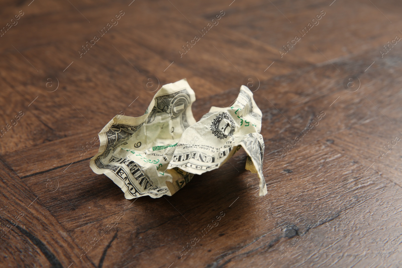 Photo of One crumpled dollar banknote on wooden table, closeup