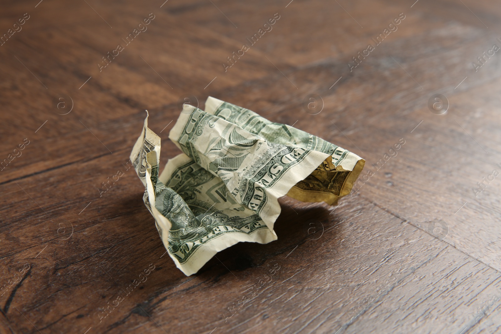 Photo of One crumpled dollar banknote on wooden table, closeup